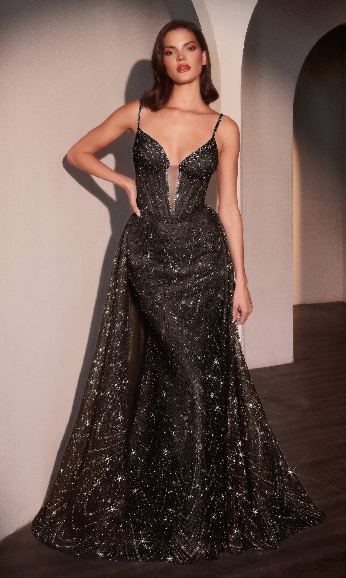 A woman stands indoors wearing the Ladivine C167, a sleeveless, floor-length black glitter prom dress with sparkling embellishments, a deep V-neckline, and a graceful mermaid skirt.